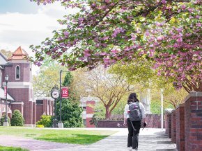 A student walks down a sidewalk under flowering trees to the right and Grace Chapel and LR banner visible to the left
