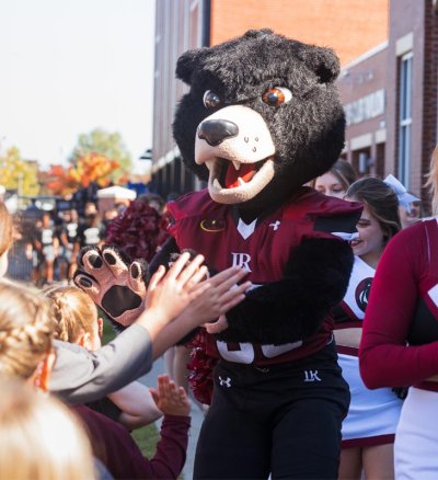 Joe Bear mascot greets childen on game day on the way to the football field