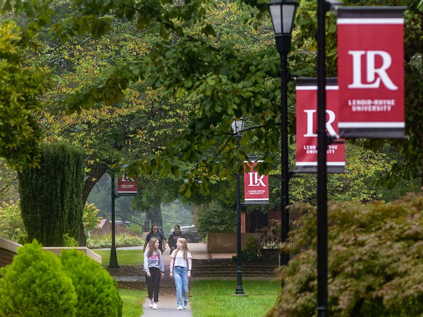 Students walking along sidewalk on campus with red LR banners on light poles