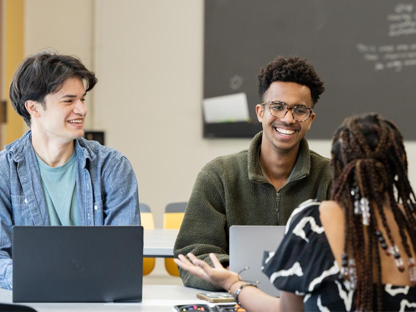 Three students sitting at table in classroom talking