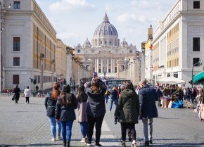 A group of students walk away from the camera toward historic buildings in Italy