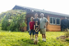 Four people stand outside in front of a house on a sunny day