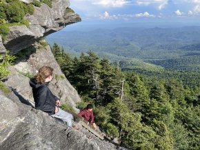 Two students lean against a rocky range overlooking mountains