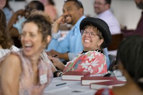 LTSS professors and alumni smiling and laughing around tables during an event.