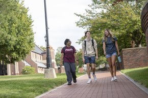 Three students walking across campus with Grace Chapel and Shaw Plaza in the background
