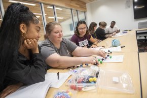 Four students assemble a diagram of a molecule at a classroom table