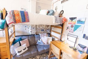 Interior of a dorm room with a sofa below loft bed, light strings and colorful throws and pillows