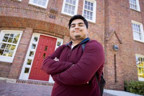 Raj Donepudi stands in front of the red main door at Mauney Hall