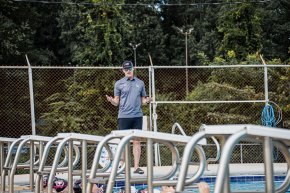 Coach Sean Weddell stands poolside and talks to a row of swimmers in the water