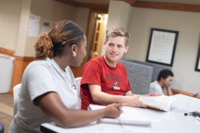 Two students look at each other while studying indoors