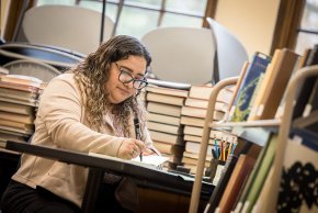 Lizbeth Santibanez works at a table surrounded by books in Rudisill Library