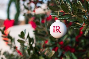 A white christmas ball with red LR logo hangs in a holly tree