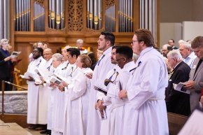 LTSS students wearing white robes stand in a row with the chapel pipe organ visible in background