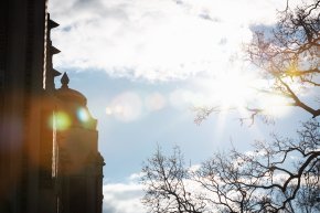 The sun shine through the clouds on a campus building roof