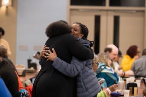 Two women hug in the dining hall during the 2024 prayer breakfast