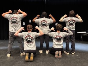 The five members of Bear With Us show the backs of their t-shirts on the stage