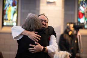 A man in clerical vestments hugs a woman with silver hair in Grace Chapel