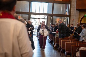 Seminary students proceed into Grace Chapel from the main entrance behind a cross on a staff.