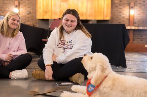 Two students sit with a fluffy golden therapy dog in Cromer Center