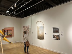 Claire Pope stands in front of her painting in an exhibit in a Mint Museum gallery