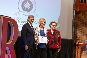 Fred Whitt, Teena Brooks and Jennifer Burris stand in front of the Tri-Alpha logo