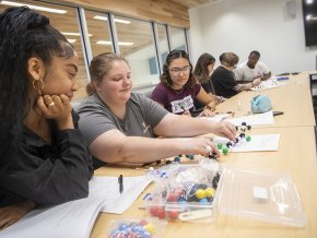 Four students assemble a diagram of a molecule at a classroom table