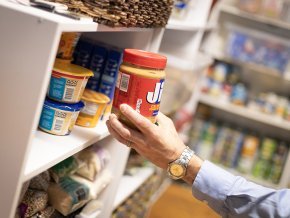 A hand places a jar of peanut butter on a shelf in the LR food pantry.