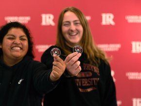 In front of red backdrop with LR logo visible, two female students hold out Bears Say Thanks stickers to foreground 