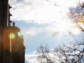 The sun shine through the clouds on a campus building roof