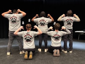 The five members of Bear With Us show the backs of their t-shirts on the stage