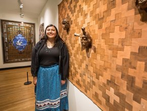 Tishara Sneed stands next to her art on exhibit, a woven design with traditional masks