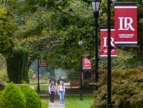 Students walking along campus sidewalk with LR red banners on light posts