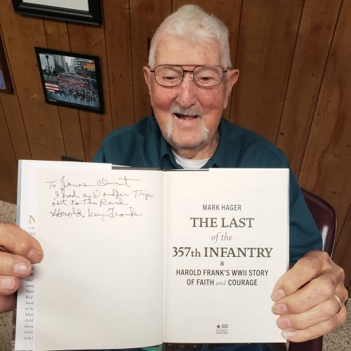 A man sits inside while holding open a book to the camera