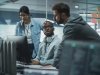 Three cybersecurity professionals review computer screens in office