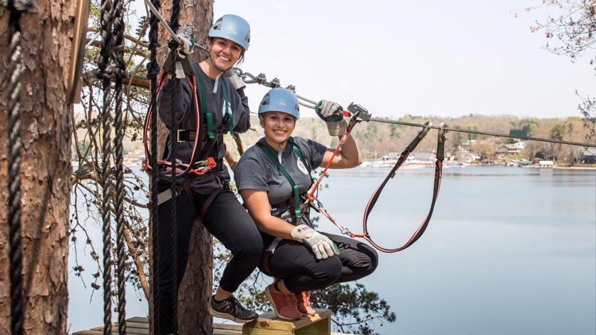 Two people getting ready to zipline by lake