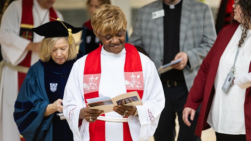 Jackie Utley in pastoral robes studies the program alongside faculty and alumni in procession at decomissioning ceremony